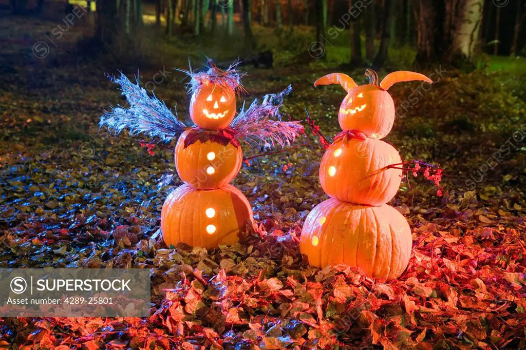 Two Jack_O_Lantern people, one angel & one devil, standing in a forest & fallen leaves on the ground at twilight during Fall in Anchorage, Alaska.