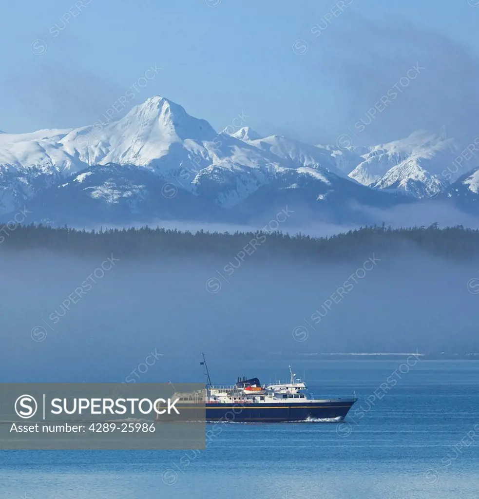 Alaska Marine Highway Ferry cruises through the misty along the Inside Passage with snowcovered peaks in the background, Southeast Alaska, Spring, COM...