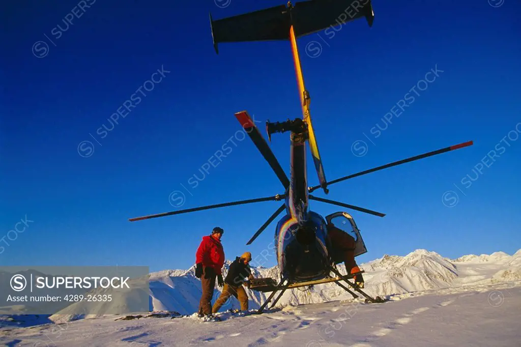 Heli_skiing crew unloads gear from helicopter atop mountain ridge Chugach Mtns Southcentral Alaska Winter