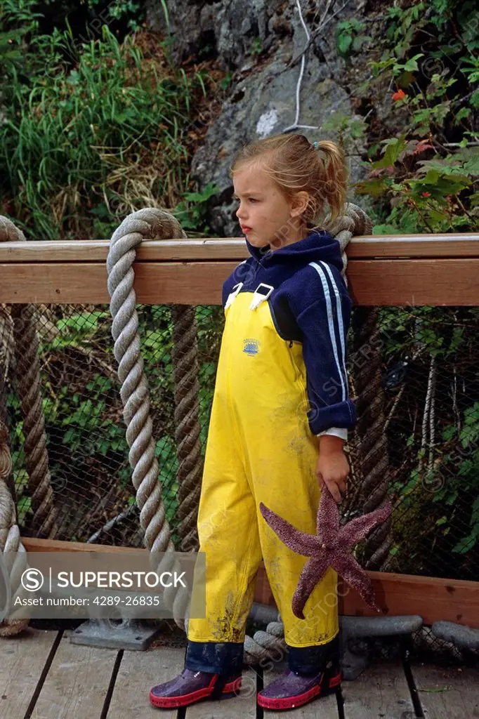Young girl in fishing overalls holding starfish at Peterson Bay Alaska