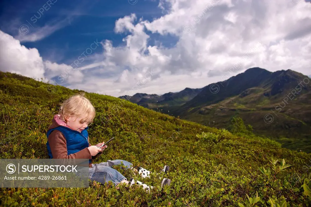 Young girl talking on a cell phone on a hillside in Hatcher Pass, Southcentral Alaska