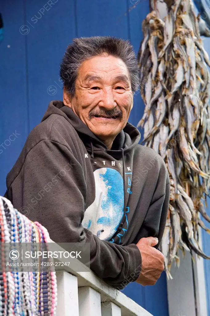 Elder native Yupik man leaning on railing off deck w/string of drying smelt Akiachak Western Alaska