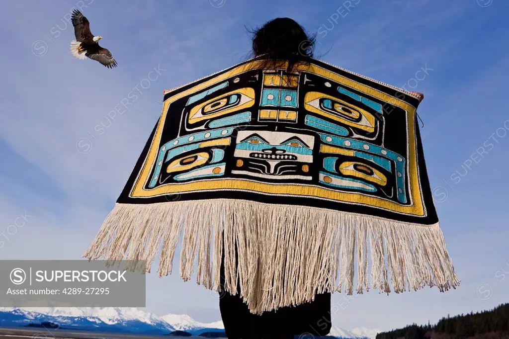 Native Alaskan wearing a Chilkat Blanket while looking upward at a soaring Bald Eagle in Alaska. Composite