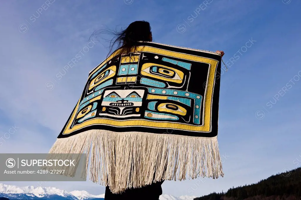 Native Alaskan wearing a Chilkat Blanket while looking upward at a soaring Bald Eagle in Alaska. Composite