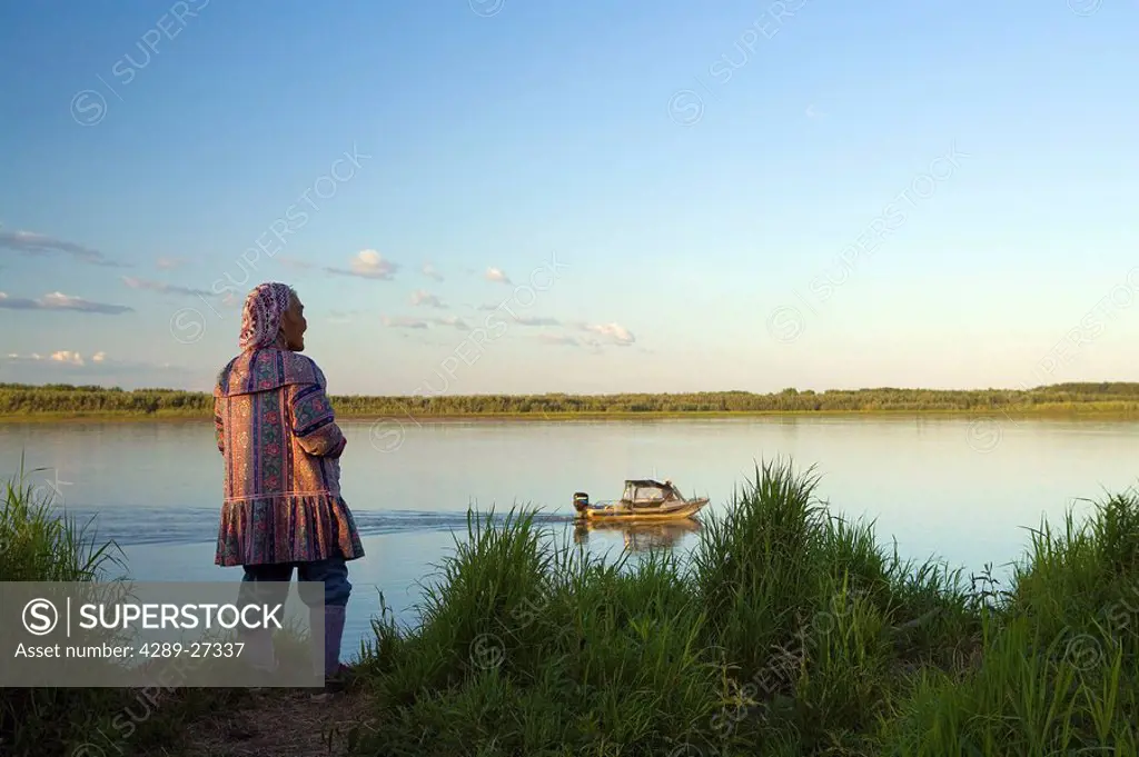 Elder native Yupik woman stands on shoreline of Kuskokwim River looking to distant WE Alaska Summer
