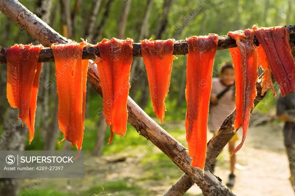 Salmon strips hung to dry on rack in fish camp while boys play in background Tuluksak Western Alaska