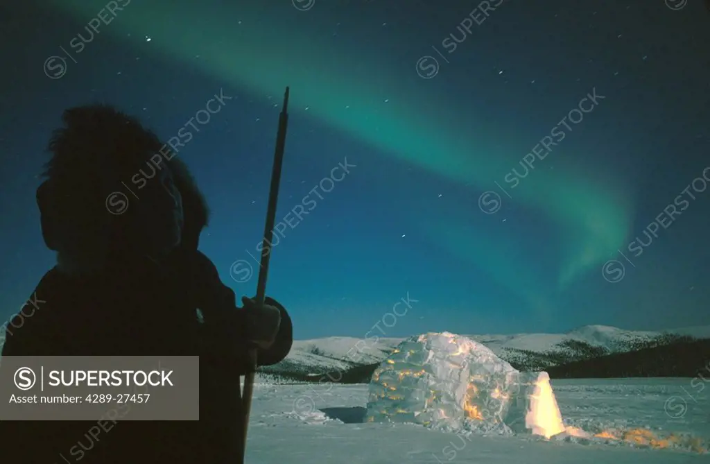 Eskimo man viewing Northern Lights over igloo Alaska composite winter scenic