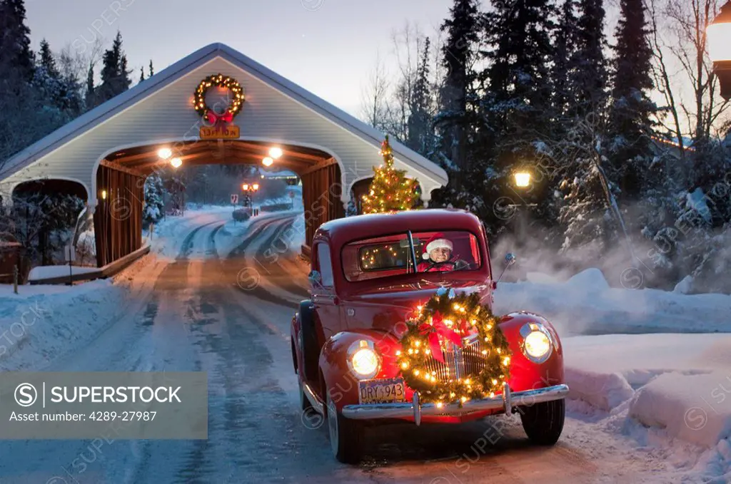 Man driving a vintage 1941 Ford pickup through a covered bridge with a Christmas wreath on the grill and a tree in the back during Winter in Southcent...