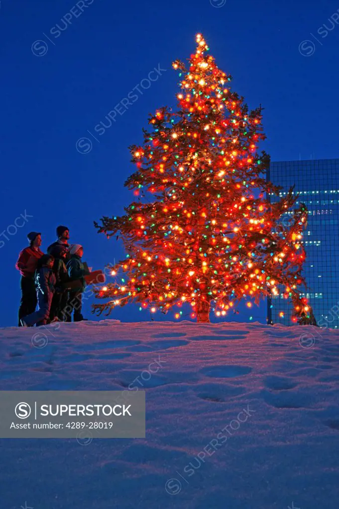 Family sings Carols under Christmas tree in City/nAnchorage Alaska