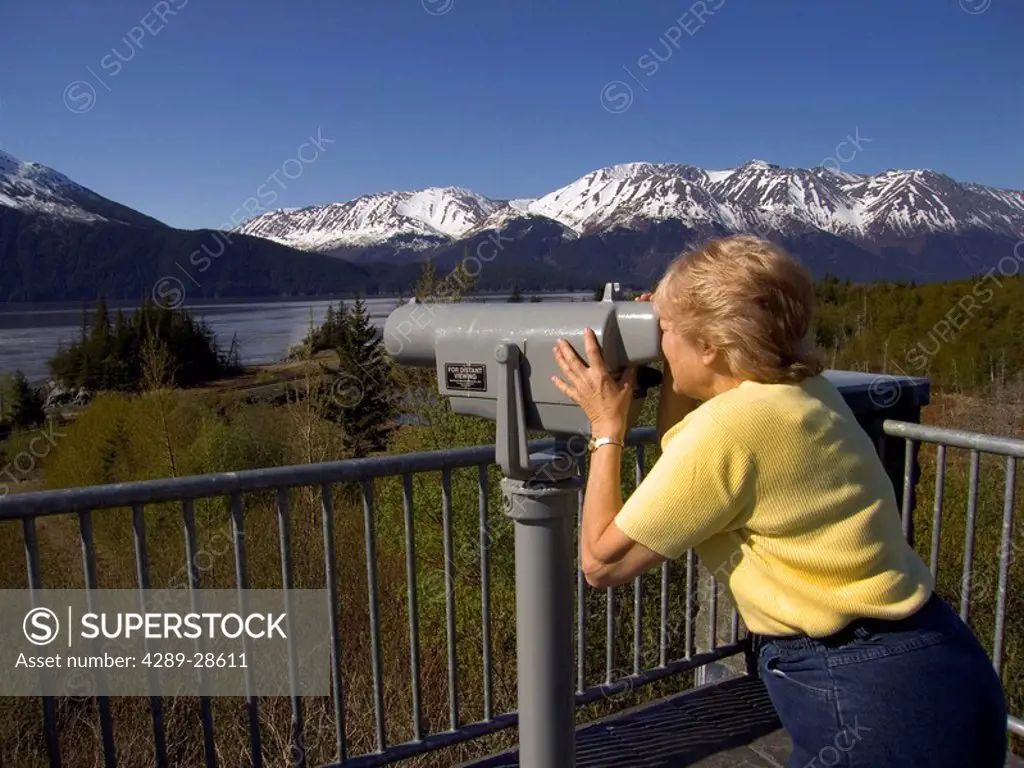 Woman looking at scenery through telescope from viewing platform Bird Point Turnagain Arm Kenai Mtns AK