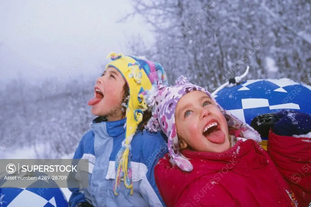 Young girls catching snowflakes on their tongues while out sledding Girdwood Alaska Southcentral Winter