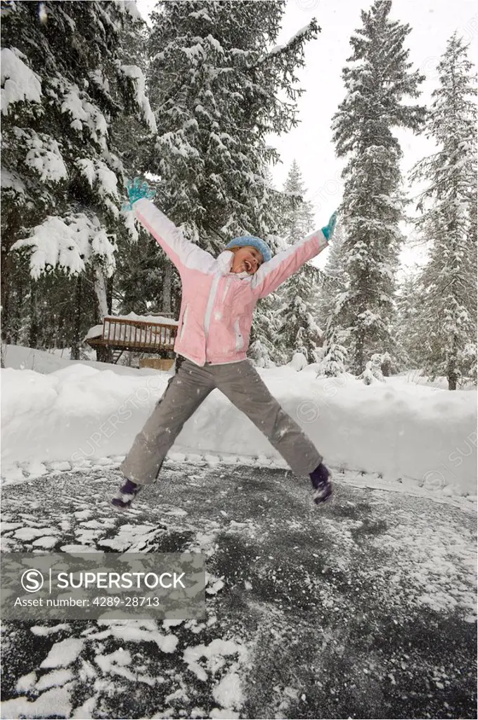 Young girl jumping on her snow covered trampoline in Girdwood, Southcentral Alaska Winter