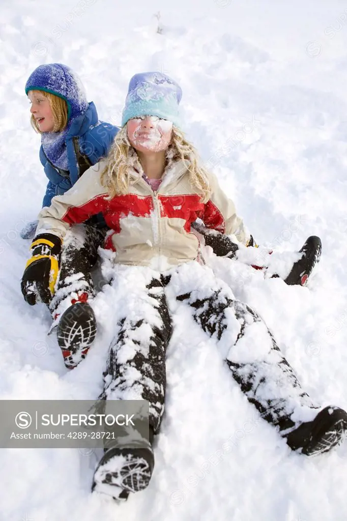 Two young girls playing in snow and sledding at Ohlson Mountain near Homer, Alaska