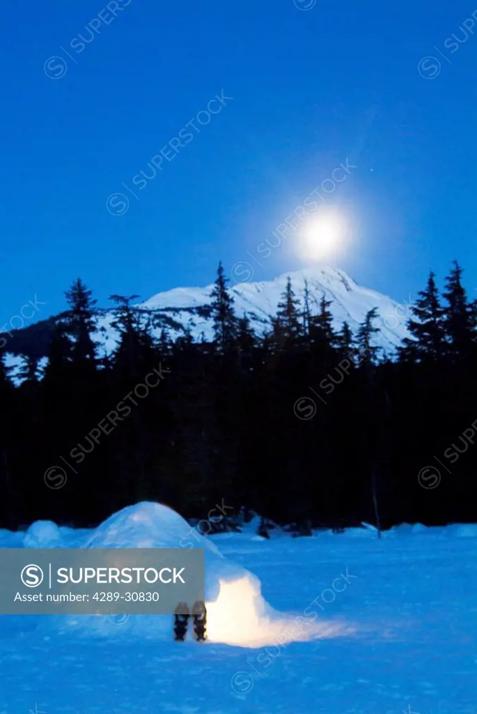 Hand built igloo in moonlight lit up with snowshoes at entrance Glacier Valley Girdwood Alaska