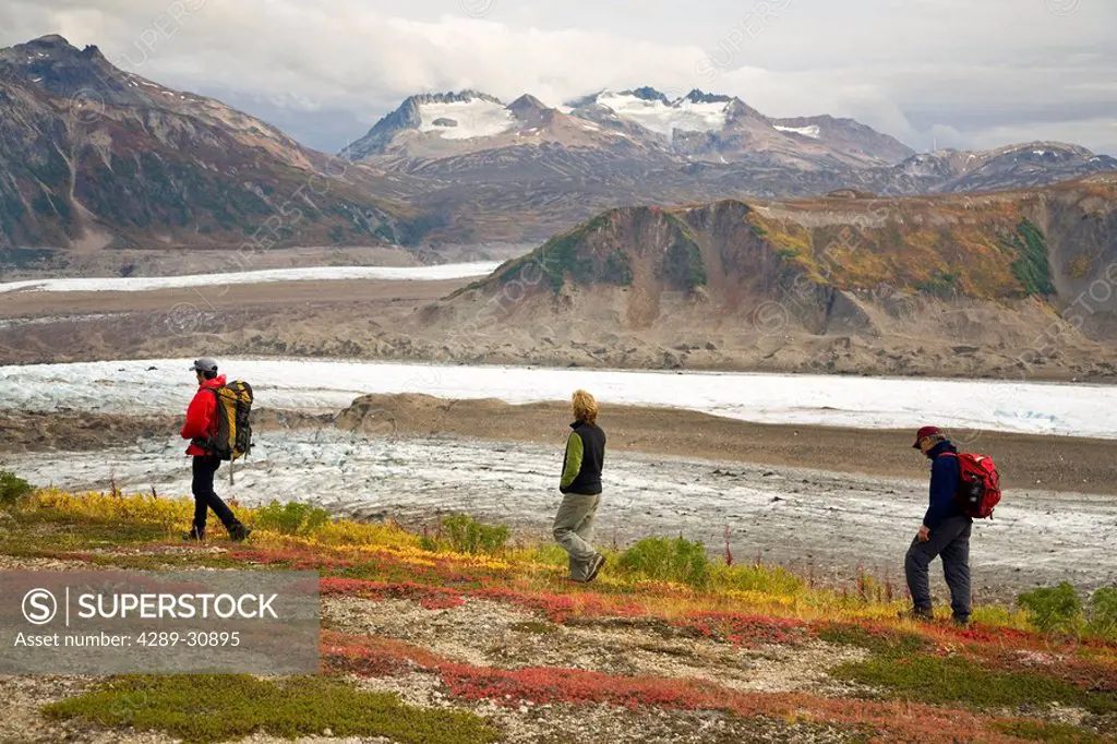 Hikers walk across a tundra ridge above the Trimble Glacier in the Tordillo Mountains. Fall in Southcentral Alaska.