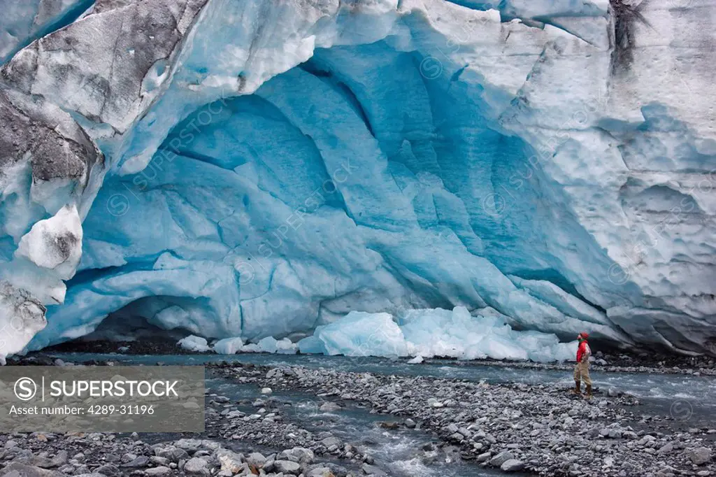 Male Hiker stands at the mouth of an ice cave formed by melt water flowing out of the bottom of Shoup Glacier, Shoup Bay State Marine Park, Prince Wil...