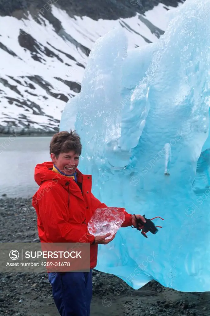 Woman holds a small chunk of ice next to a large grounded iceberg at Reid Inlet in Glacier Bay National Park in Southeast Alaska