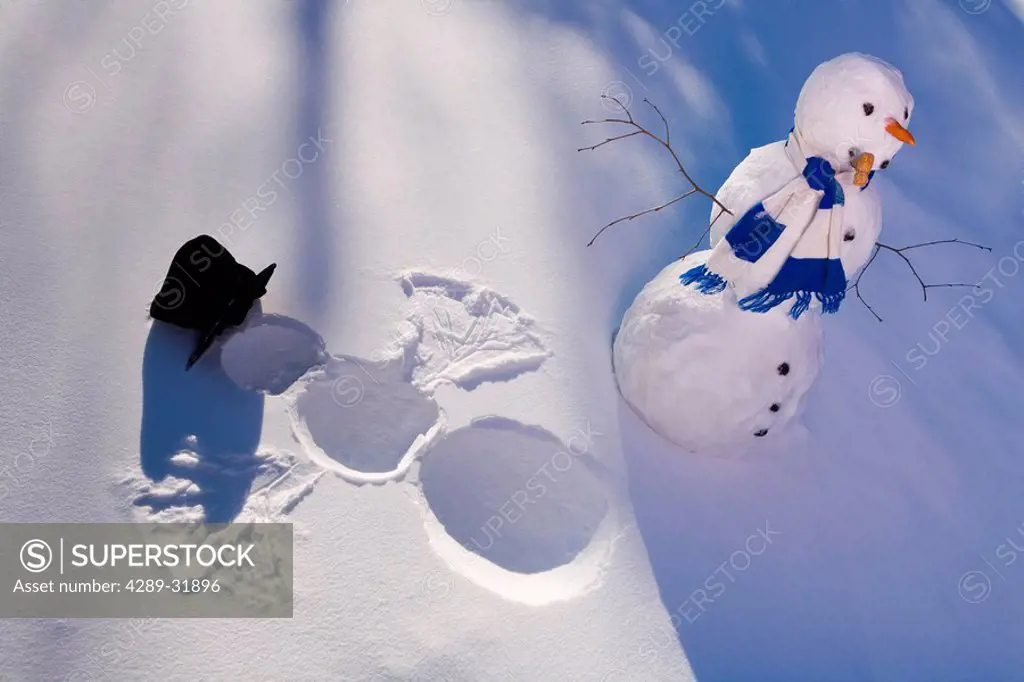Snowman in forest making snow angel imprint in snow in late afternoon sunlight Alaska Winter