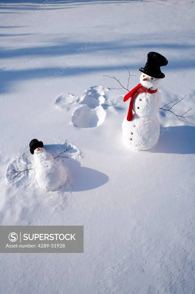 Snowmen in forest making snow angel imprint in snow in late afternoon sunlight Alaska Winter