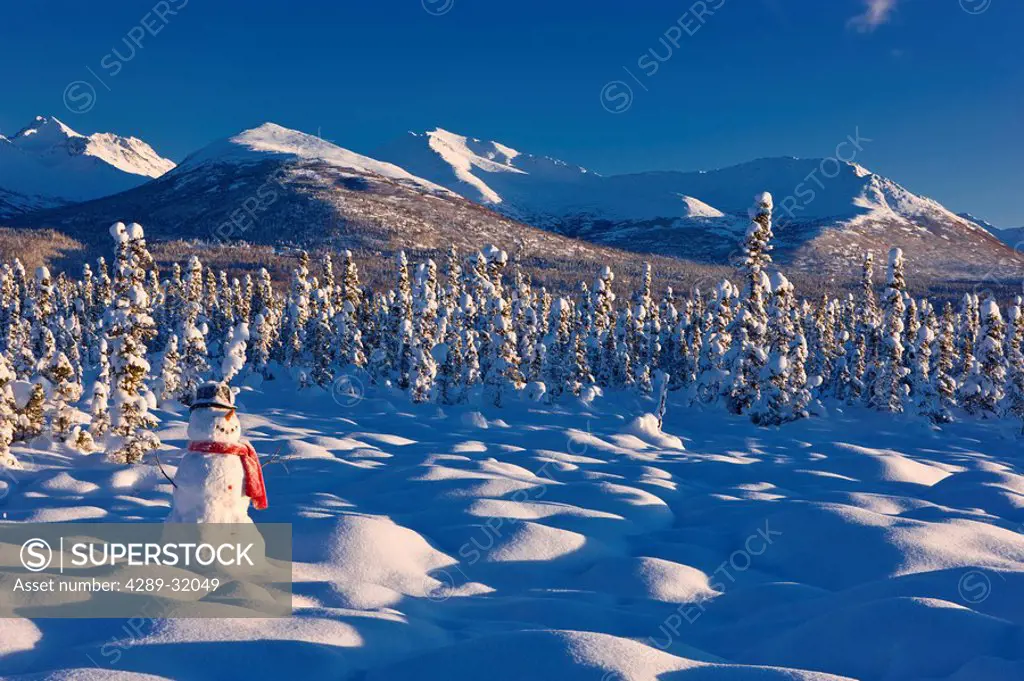 A snowman standing in snow covered tundra at sunset, spruce forest and Chugach Mountains in the background, winter, Anchorage, Alaska