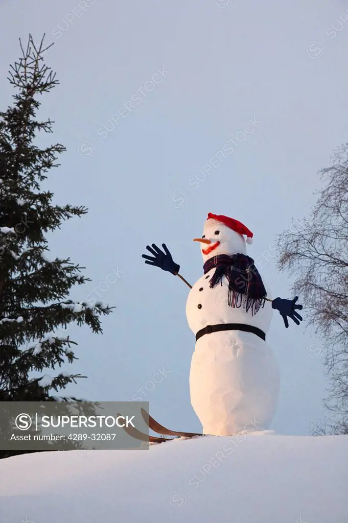 A snowman fitted with a santa hat, gloves, and skiis is perched on a small snow covered knoll in Anchorage, Southcentral Alaska