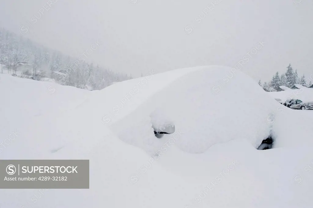 A small car is buried in deep snow at the base of Alyeska Ski Resort during a snow storm, Girdwood, Southcentral Alaska, Winter