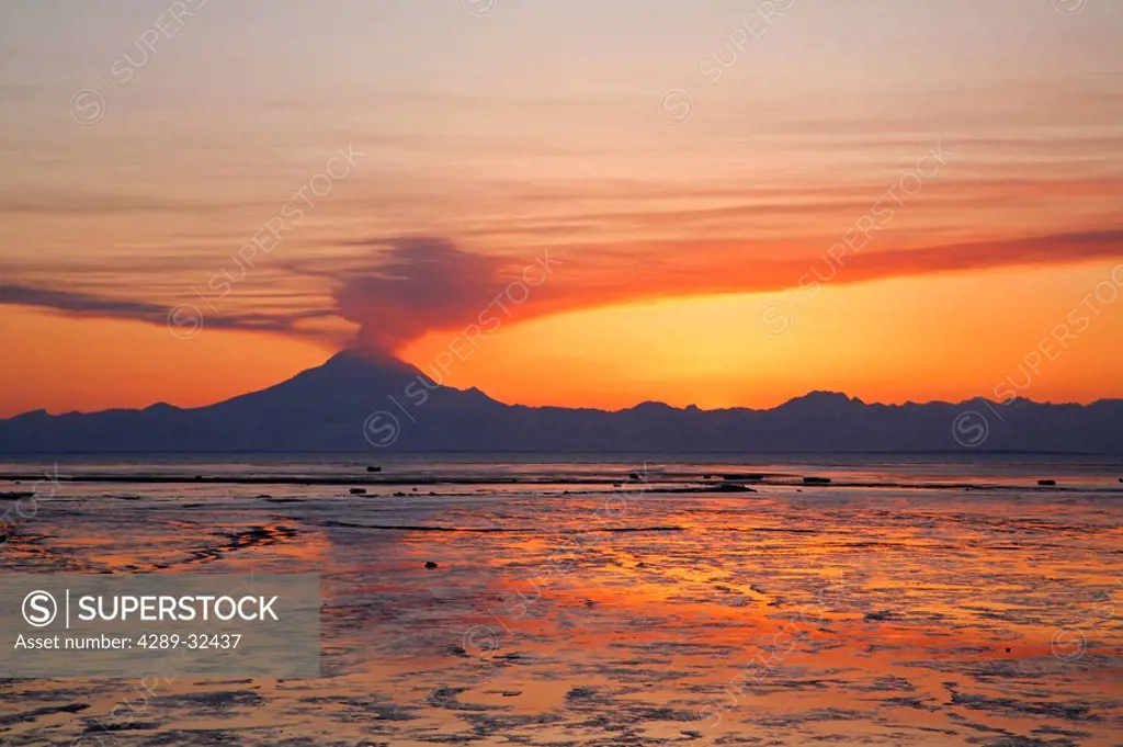 Ash cloud rises from Mt. Redoubt at sunset during low tide near Ninilchik, Alaska