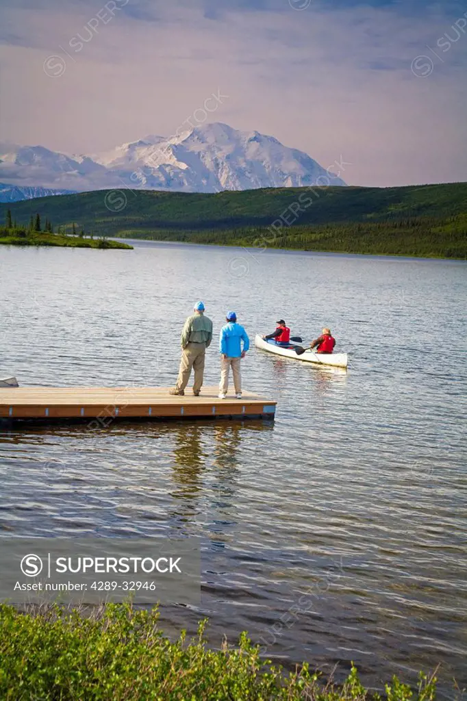 Mature couples canoe on Wonder Lake as others watch from dock with Mt. Mckinley in background, Denali National Park, Alaska