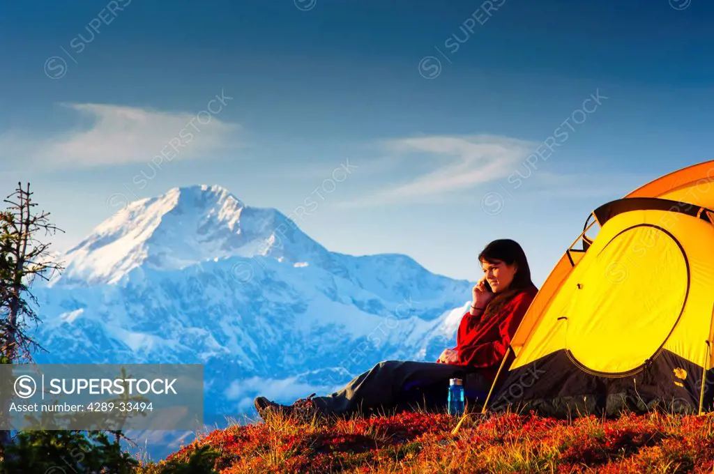Woman talking on her cell phone while camping with the south summit of Mt. McKinley in the background, Peters Hills, Denali State Park, Southcentral A...