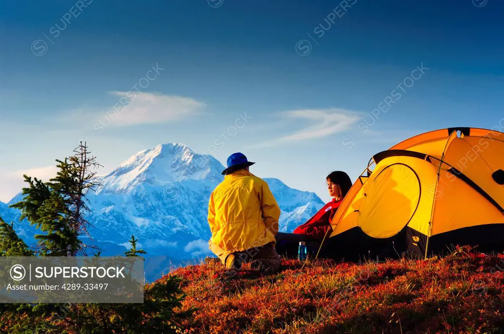 A man and woman sitting by their tent in Peters Hills with Mt. McKinley in the background, Denali State Park, Southcentral Alaska, Fall/n