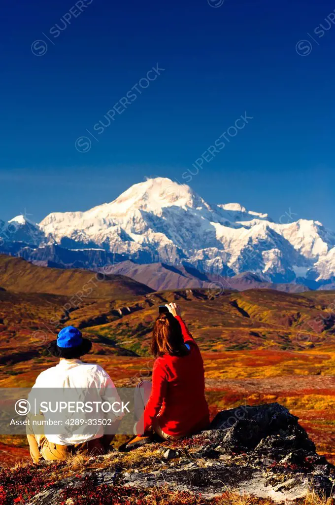 A couple hiking in Peters Hills stop to take a picture of Mt. McKinley with a cell phone, Denali State Park, Southcentral Alaska, Fall/n