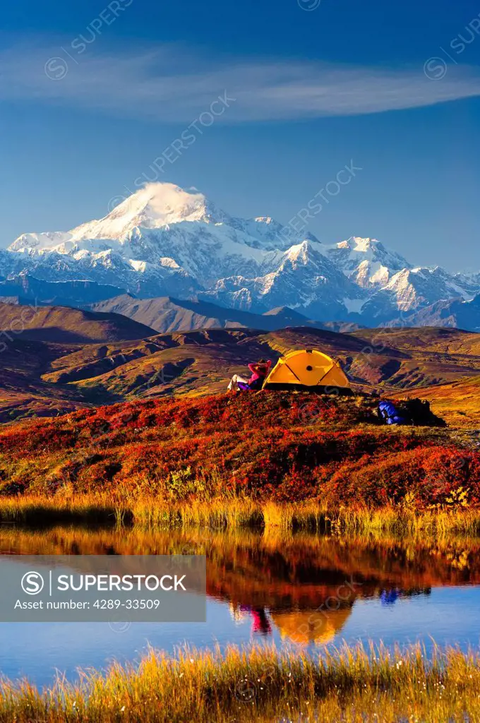 A couple relaxes next to their tent in Peters Hills with a view of Mt. McKinley in the background, Denali State Park, Southcentral Alaska, Fall/n