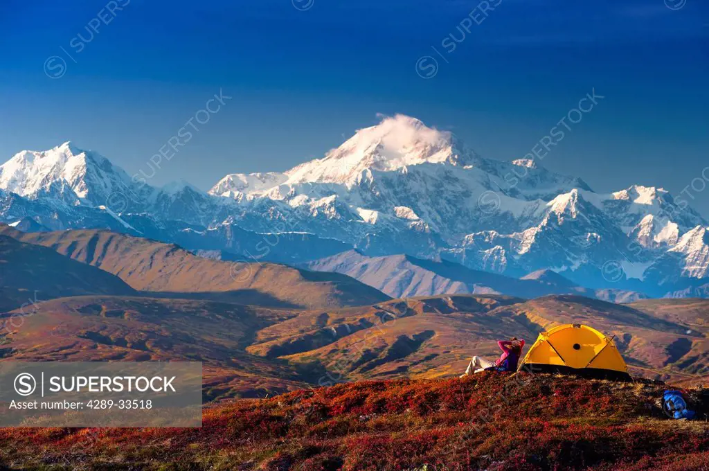 A woman relaxes next to her tent in Peters Hills with a view of Mt. McKinley in the background, Denali State Park, Southcentral Alaska, Fall