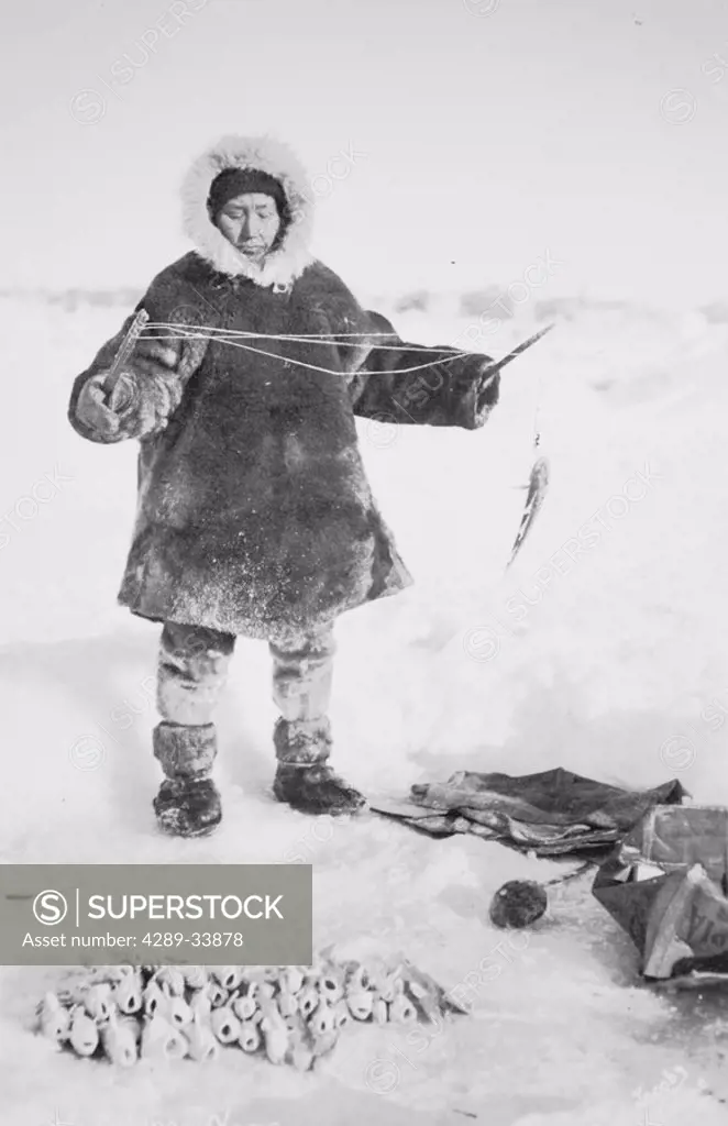 Historical image of person dressed in a native parka and mukluks ice fishing winter Alaska