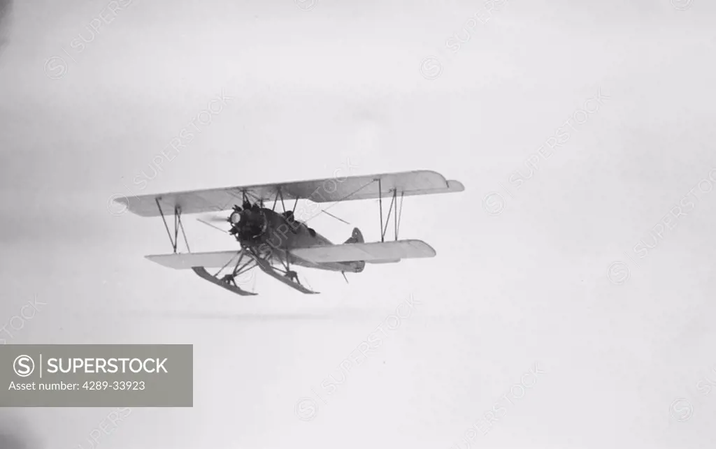 Historical image of a flying biplane on skis Alaska