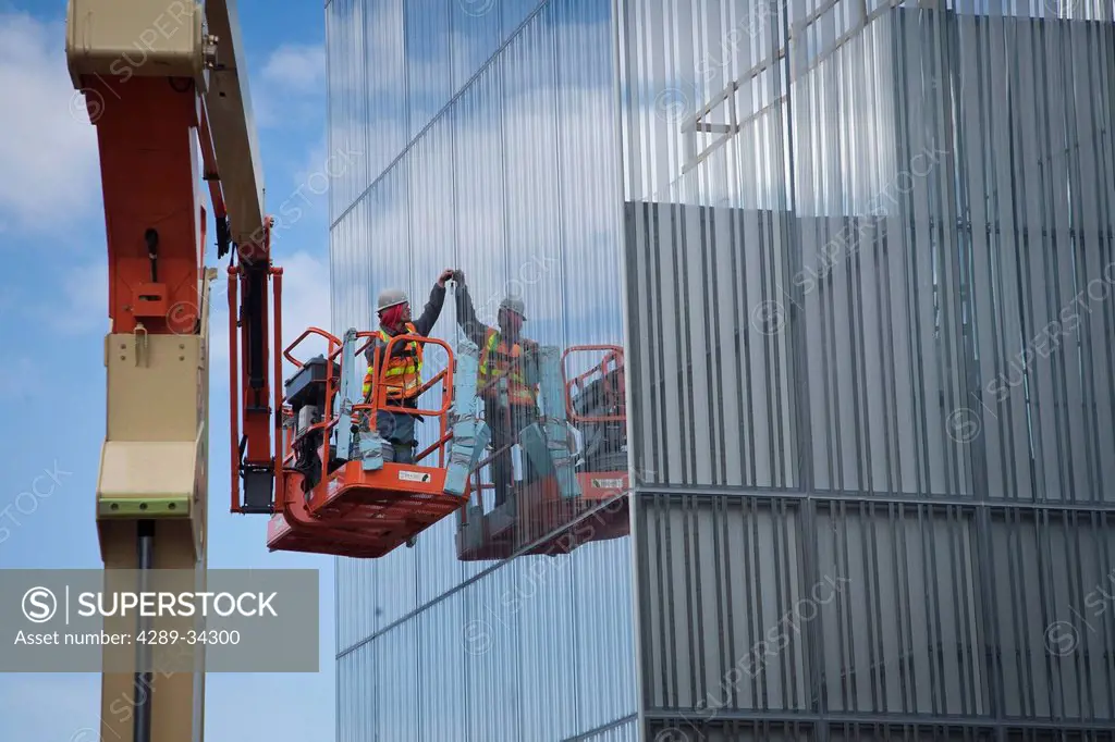 Male glazer installs glass fom a man lift on the exterior of the Anchorage Museum addition during construction, Anchorage, Southcentral Alaska, Spring