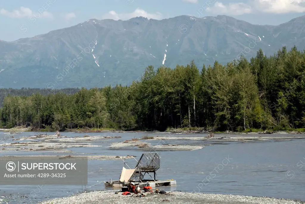 Two men relax on a gravel bar next to an aluminum fish wheel on the Matanuska River, Mat_Su Valley, Southcentral Alaska, Summer