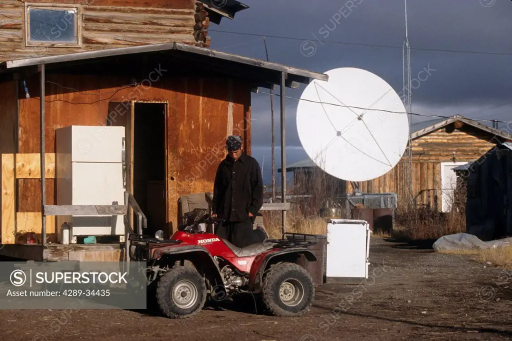 Native man stands next to an ATV on an Autumn day in Arctic Village, Arctic Alaska