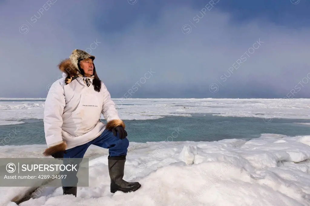 Male Inupiaq Eskimo hunter standing on a ice pressure ridge while wearing a traditional Eskimo parka Atigi and seal skin hat, Chukchi Sea near Barrow,...