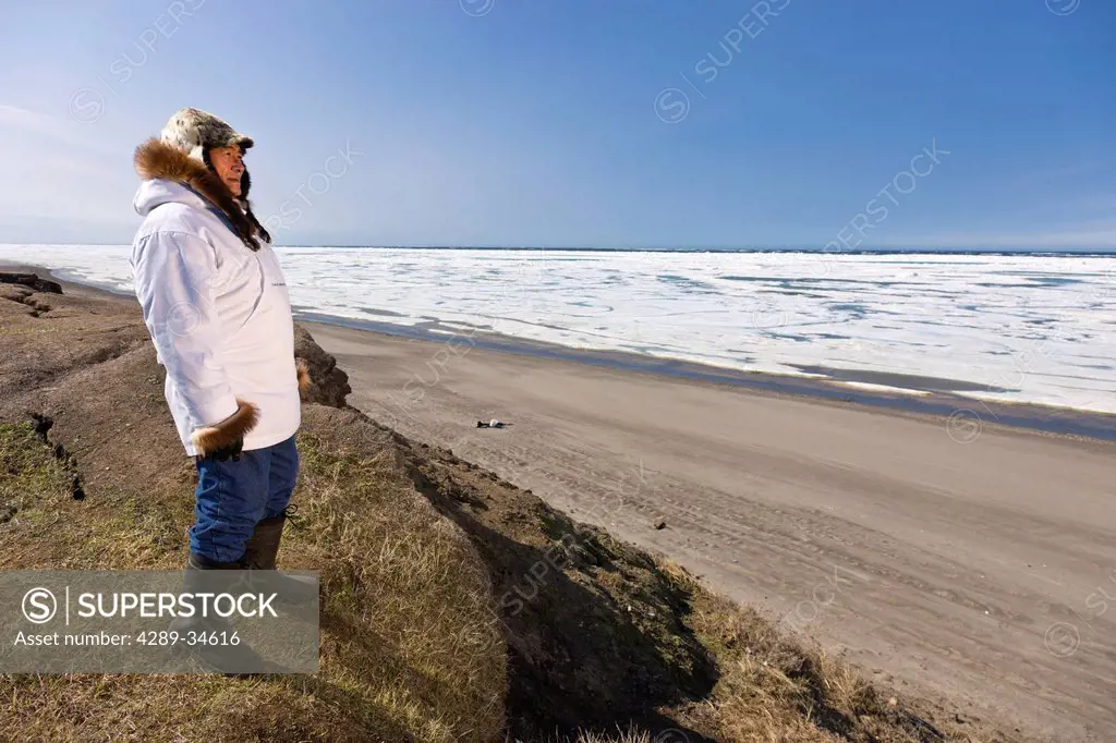 Portrait of a male Inupiaq Eskimo hunter wearing his Eskimo parka Atigi and seal skin hat while standing at Old Utkeagvik original town site overlooki...