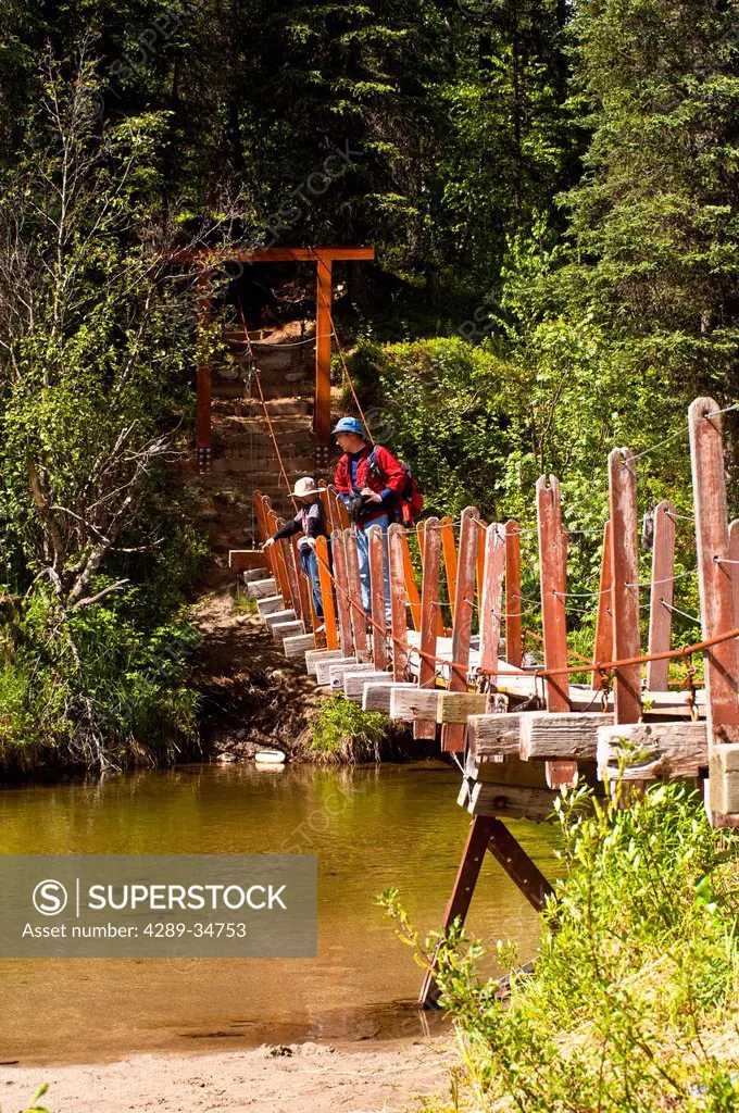 A father and son hiking across a suspension bridge that crosses Byers Creek on the Byers Lake Trail in Denali State Park, Southcentral Alaska, Summer