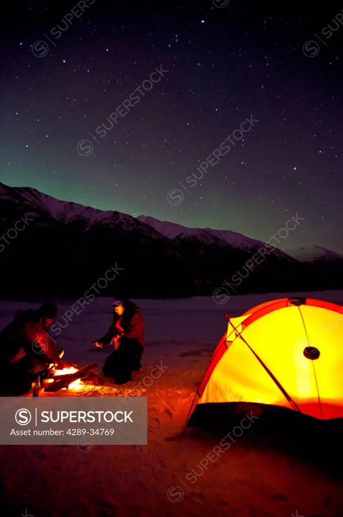 Two men camp on the frozen Eklutna Lake with the Northern Lights overhead, Chugach State Park, Southcentral Alaska, Winter