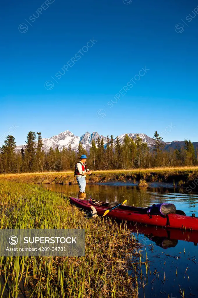 Man with a kayak fishing from the shore of Rabbit Slough in the Palmer Haystack Flats wildlife refuge, Matanuska_Susitna Valley, Southcentral Alaska, ...