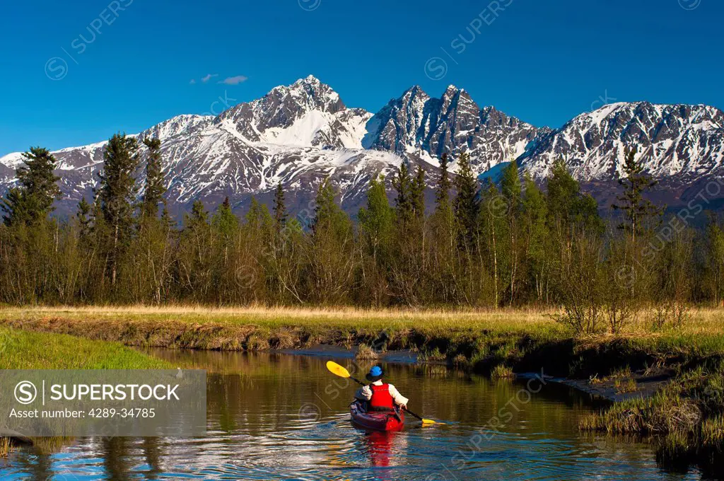 A man kayaking on Rabbit Slough in Palmer Haystack Flats Wildlife Refuge on a sunny spring day in the Matanuska_Susitna Valley, Southcentral Alaska