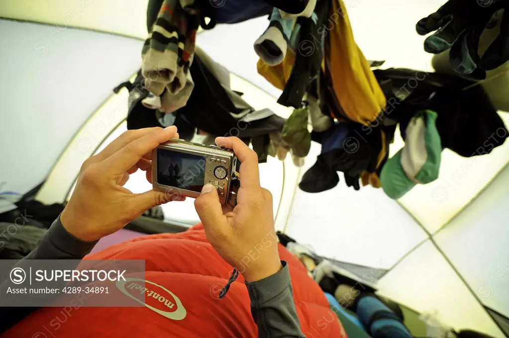 Female climber looks at photos on her digital camera in her tent at Kahiltna Base Camp on the West Buttress Route, Denali National Park and Preserve, ...