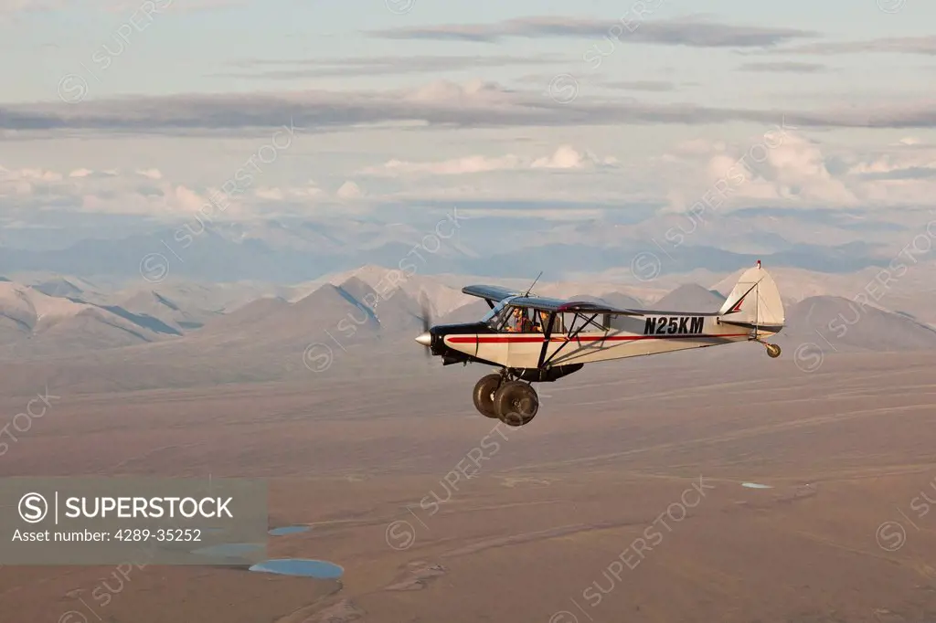 Aerial view of a Piper Super Cub airplane flying over the Jago River and tundra of the coastal plain in ANWR with the Romanzof Mountains in the backgr...