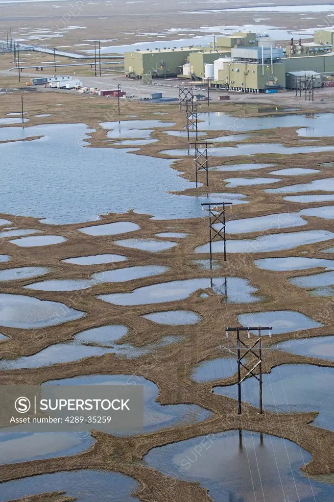 Aerial view of electric transmission lines over pond covered tundra leading to an oil development structure in the Prudhoe Bay oil field, Arctic Alask...