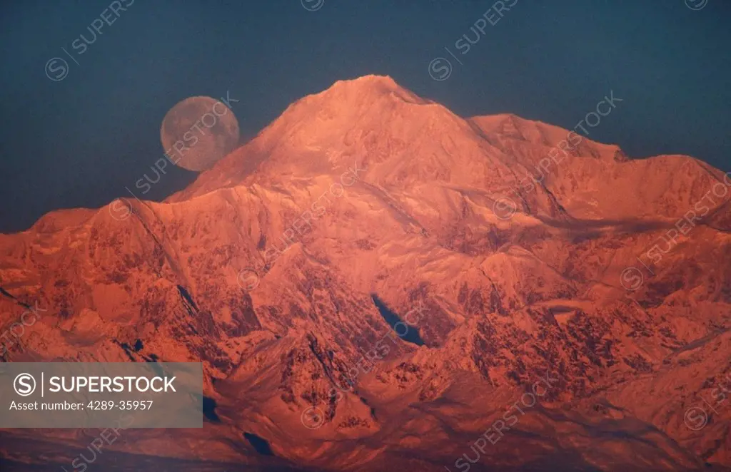 The full moon sets behind Mt. McKinley lit by alpenglow at sunset, near Talkeetna, Southcentral Alaska