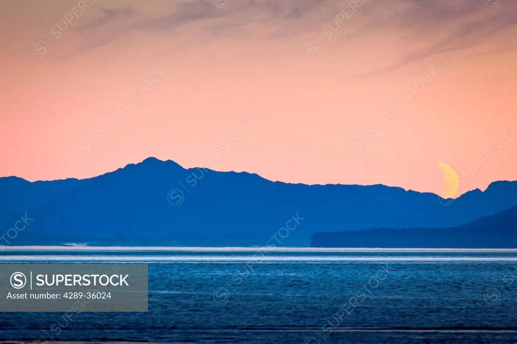 Scenic view at dawn of a crescent moon setting behind coastal mountains, Icy Strait, Glacier Bay National Park & Preserve, Southeast Alaska, Summer