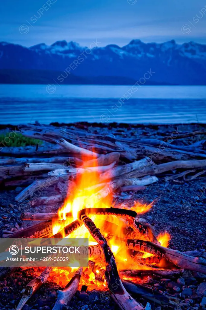 Campfire at dusk on a remote coastal beach in Goose Cove with Fairweather Range in the background, Muir Inlet, Glacier Bay National Park & Preserve, S...